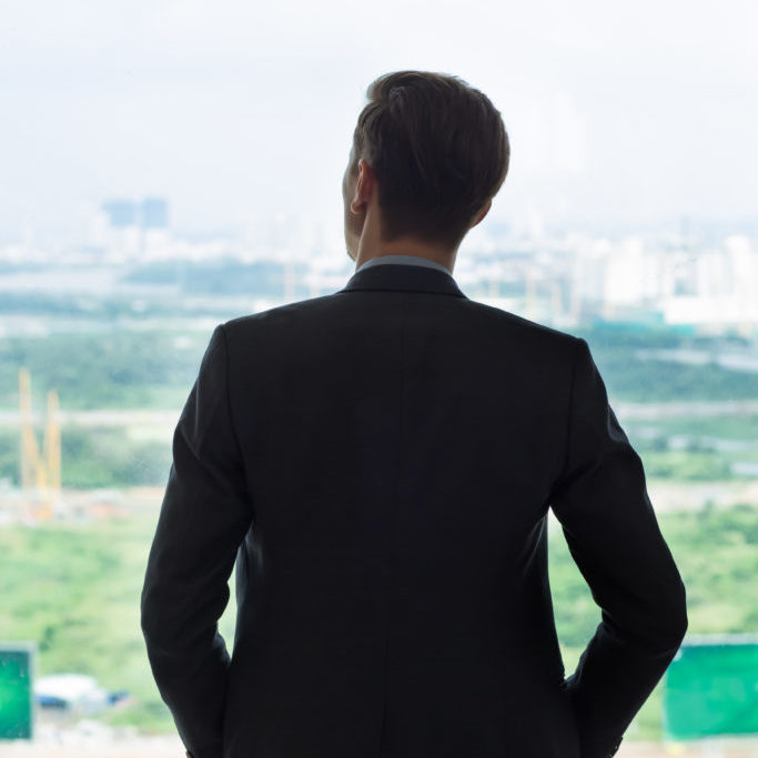 Back view of young businessman standing by window, enjoying city view